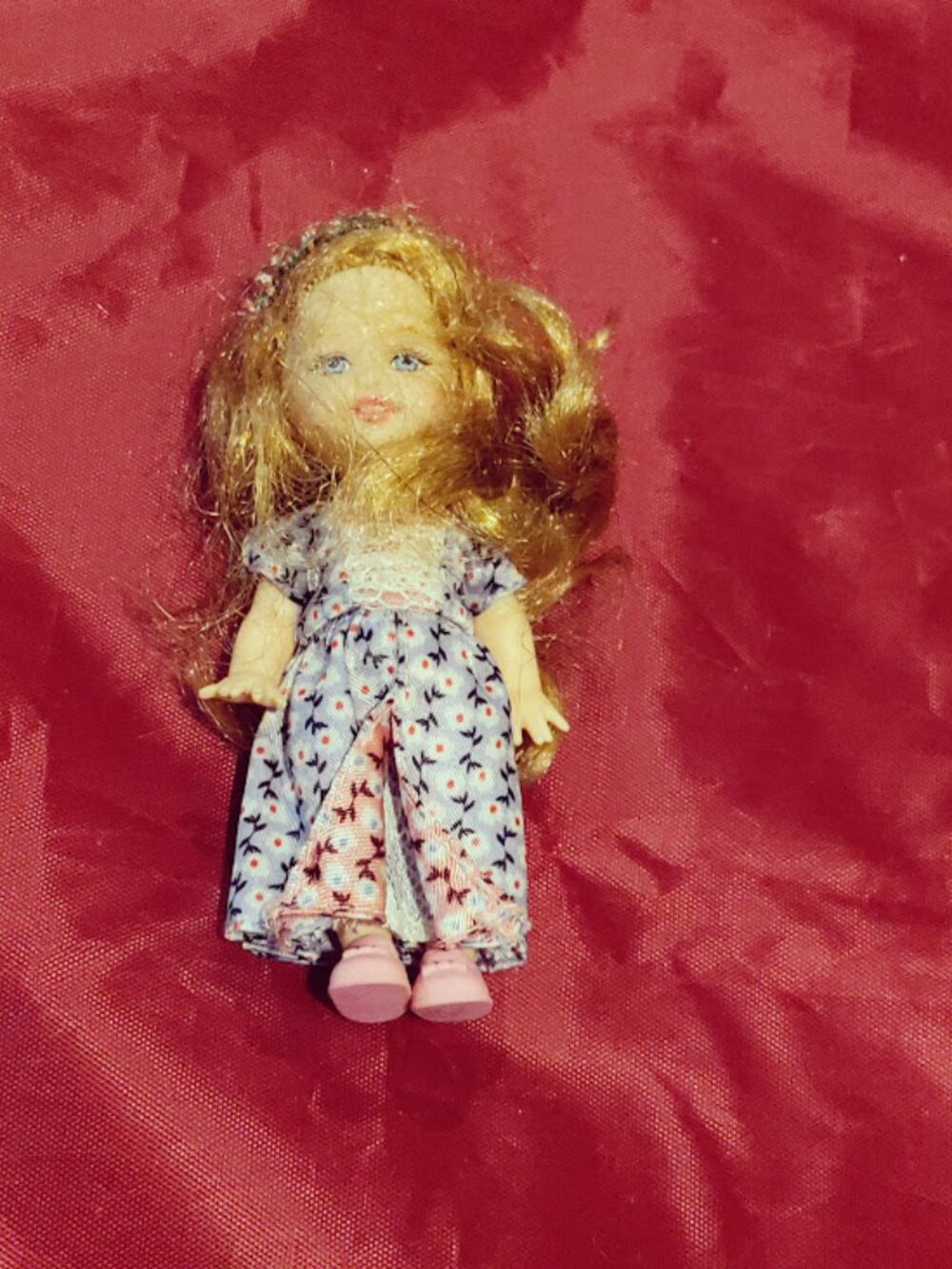 Small red-haired mini doll wearing a purple and gold princess-style dress with p